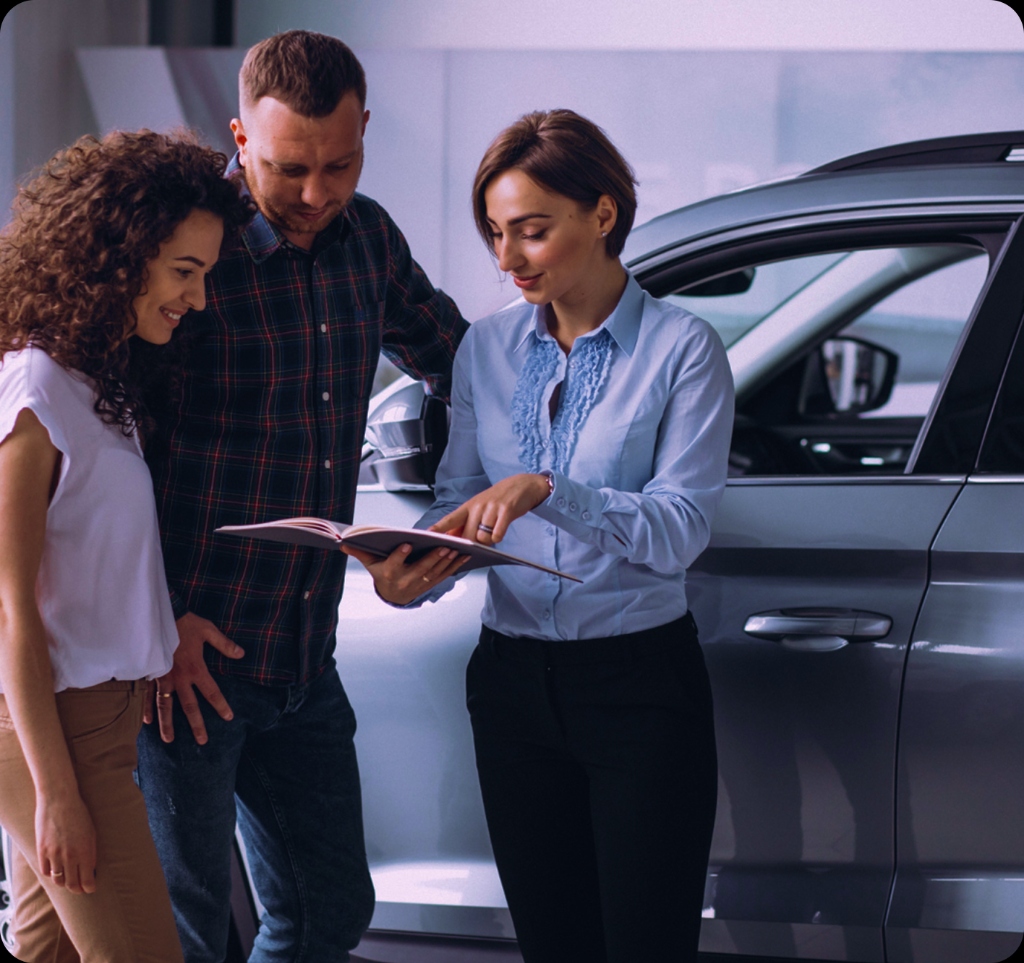 Three people reviewing a document in a showroom next to a vehicle